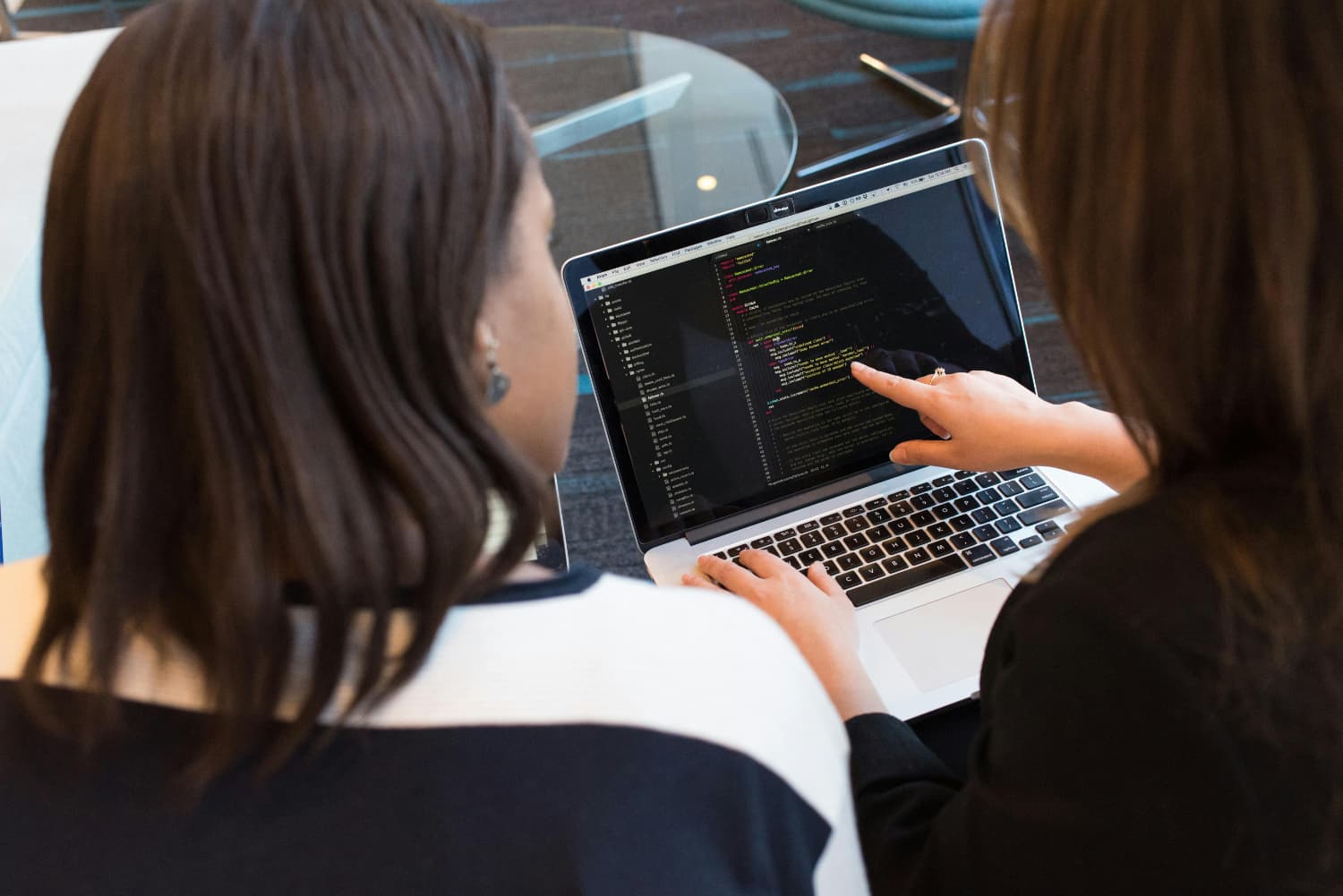 Two women are looking and pointing at a computer screen with code on it.