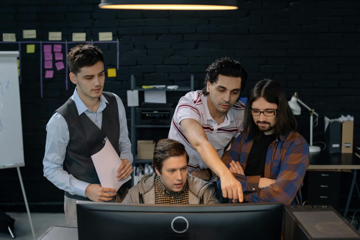 A group of men are discussing and pointing at a computer monitor.